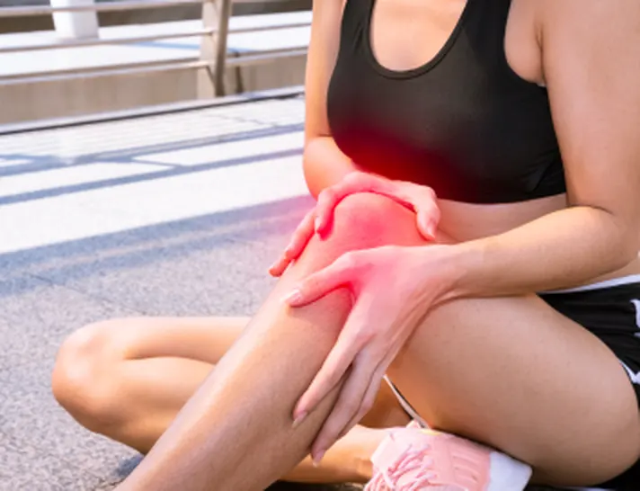 Mujer sentada sujetándose la rodilla, con la zona del dolor marcada